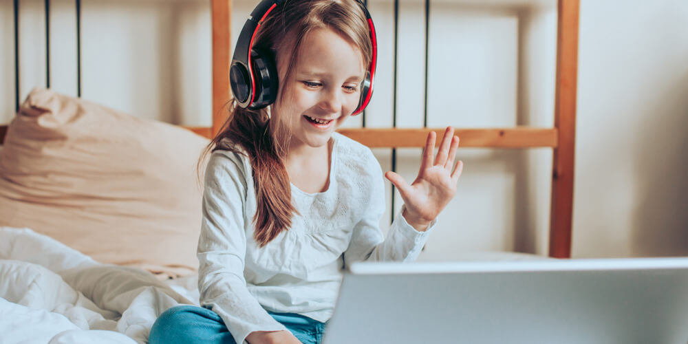 Student-online-first-image An elementary school student smiles and waves while attending a virtual class on her laptop