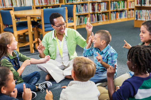 Teacher sitting with students on the floor while singing and dancing